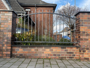 Geschmiedeter Zaun mit handgefertigten Spitzen und sichtbaren Nieten, montiert zwischen Backsteinpfosten.