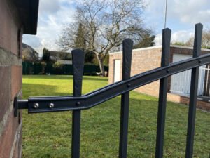 Detailaufnahme der Befestigung des geschmiedeten Zauns an der Backsteinmauer, mit sichtbaren Nieten und handgefertigten Elementen.