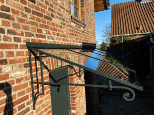 Aus der Vogelperspektive: ein grünes Glasvordach, freitragend montiert an einer roten Backsteinmauer – ein spannendes Farbspiel aus Glas und Ziegel.