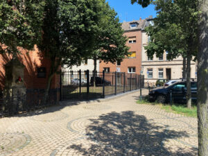 Blick auf den modern gestalteten, vernieteten Metallzaun mit dekorativen Schmiedeteilen vor einer Backsteinkirche.